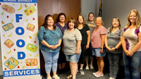 Teachers standing next to a School District Food Services sign
